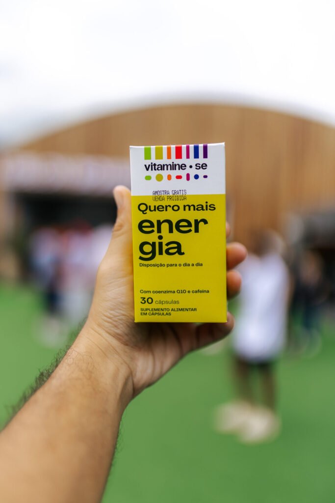 Caixa do suplemento Quero Mais Energia, da linha Vitamine-se da EMS, segurada em frente ao stand no Rio Open 2026