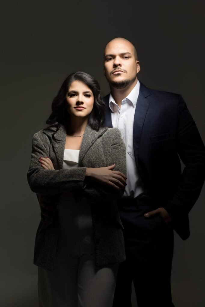 Retrato corporativo de casal de corretores em estudio com fundo escuro e luz dramatica